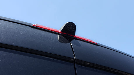 Rearview camera and red third brake light on top of a black RV rental van for safer driving.