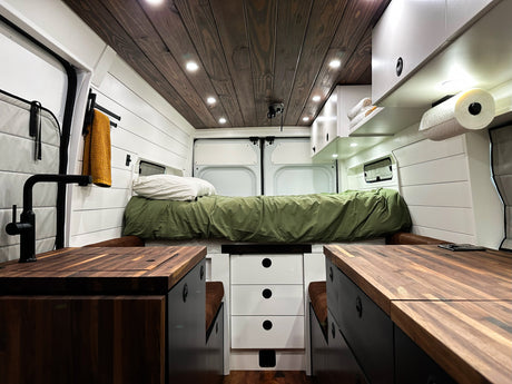 Stylish camper van RV rental interior: wood ceiling, white walls, built-in kitchen, seating, and bed for adventures.
