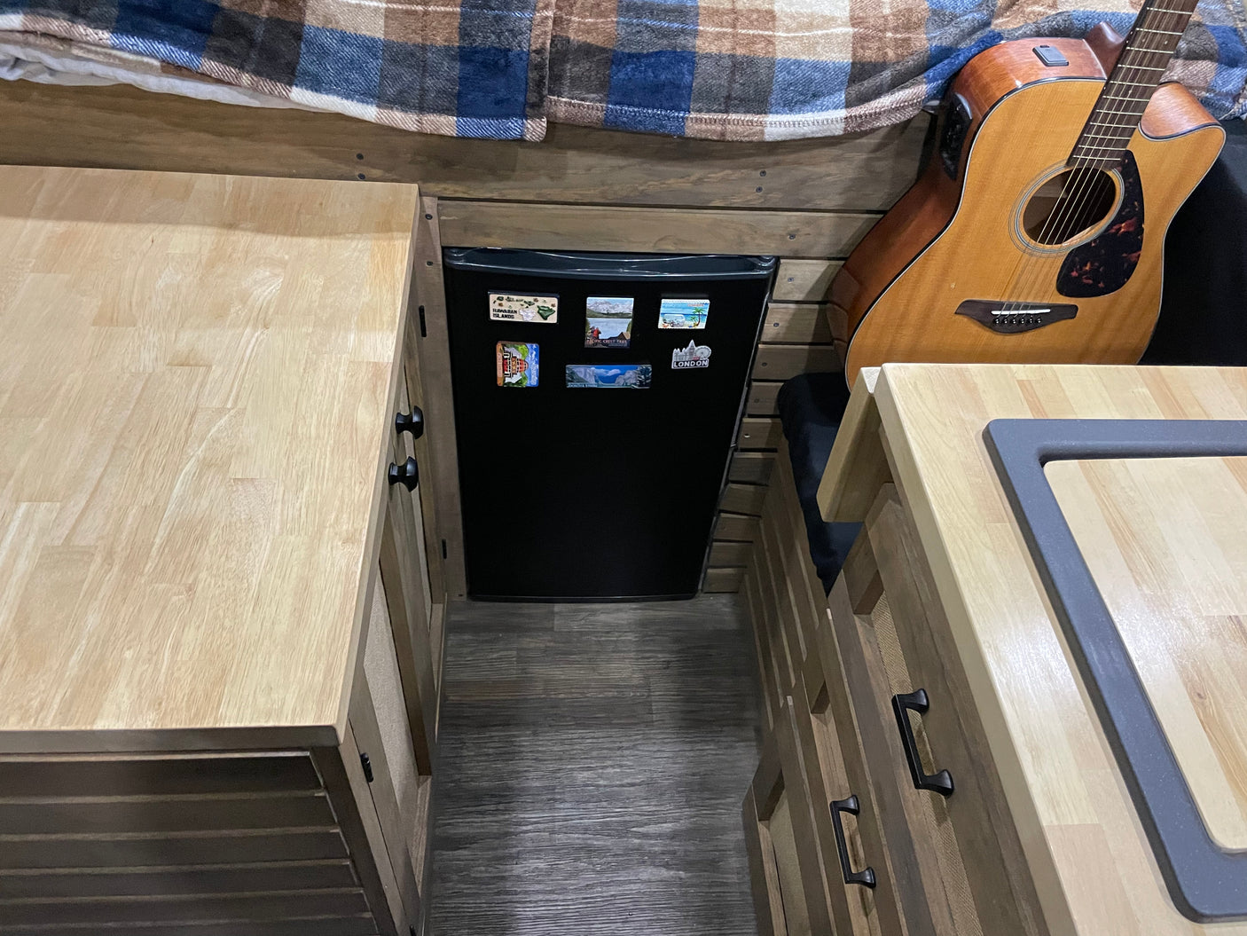 Explore this RV rental's cozy interior, featuring custom wood counters, a mini-fridge, and an acoustic guitar.