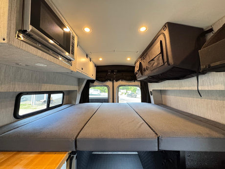 Comfortable RV rental interior with a large folding bed, microwave, and overhead storage. Ready for your next adventure!