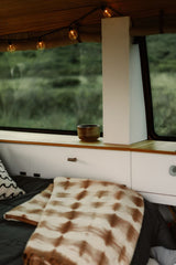 Cozy RV rental interior with comfy bed, warm string lights, and a window view of lush green hills. Ideal for travel.
