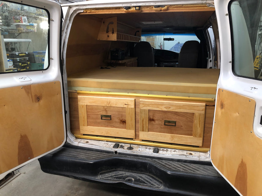 This RV rental camper van features a custom wood interior with a bed, drawers, and overhead storage, ready for adventure.