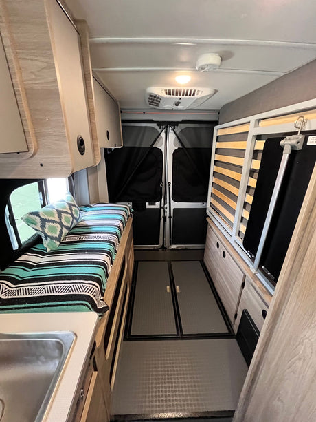 Cozy RV rental interior with a vibrant bed, practical sink, and smart storage, offering comfort for travel.