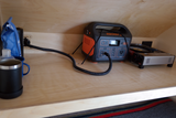 A Jackery portable power station powers a cozy RV rental setup with a portable stove & coffee gear inside a wooden cabinet.