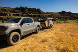 This rugged GMC Sierra AT4X tows an Escapapod teardrop RV rental trailer through dry, rocky landscapes.