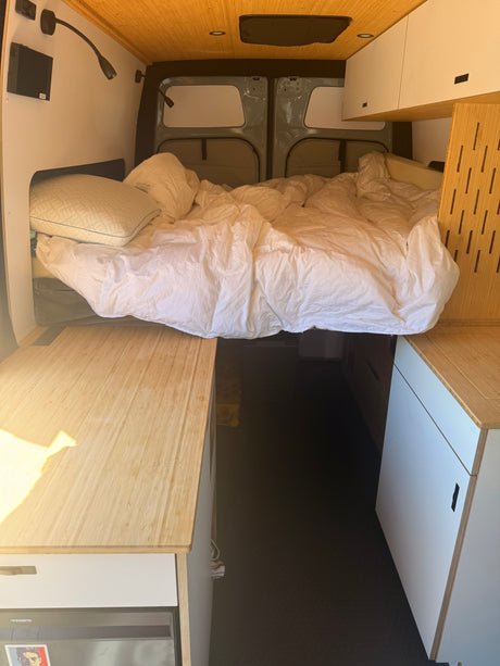 Inside a modern RV rental camper van: comfortable bed, bamboo counters, storage, and Dometic fridge for adventures.
