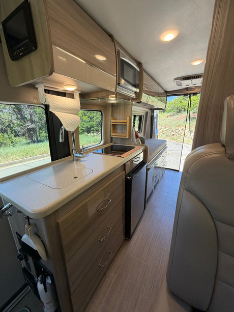RV rental interior: compact kitchenette with sink, cooktop, microwave, fridge, and rear sleeping area, ideal for road trips.