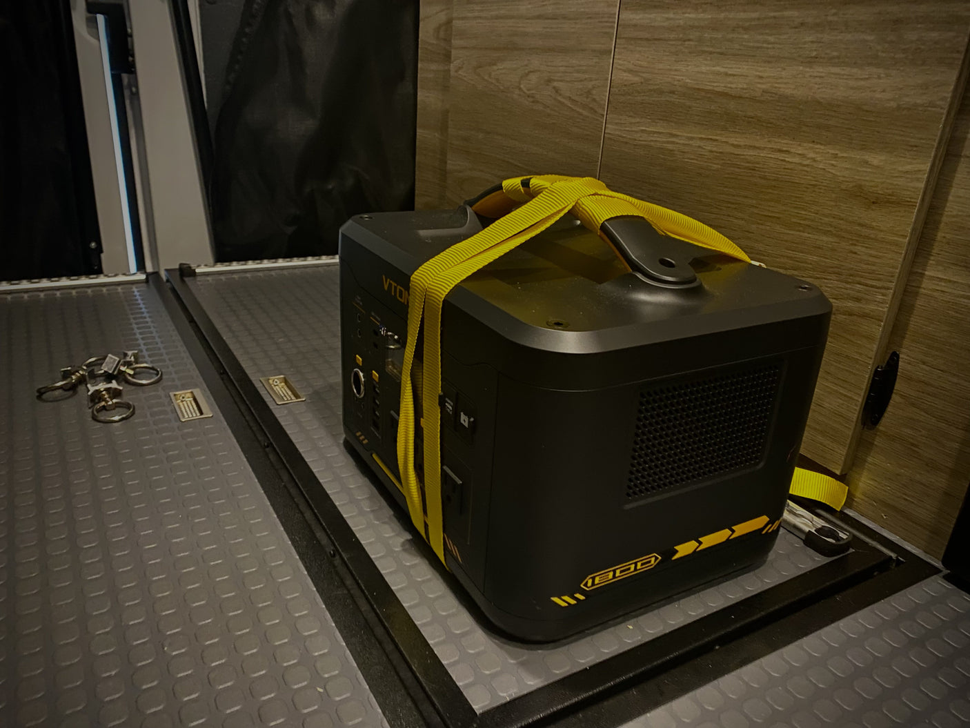 A VTON 1500 portable power station is securely strapped in an RV rental, on a textured floor with cargo rails.