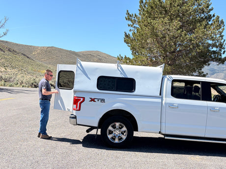 Man opens his white truck camper, an excellent RV rental for exploring. The XTR 4x4 pickup is ready for adventure.