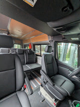 Inside an RV rental: versatile van interior with black leather seating, movable floor tracks, and cozy wood ceiling.