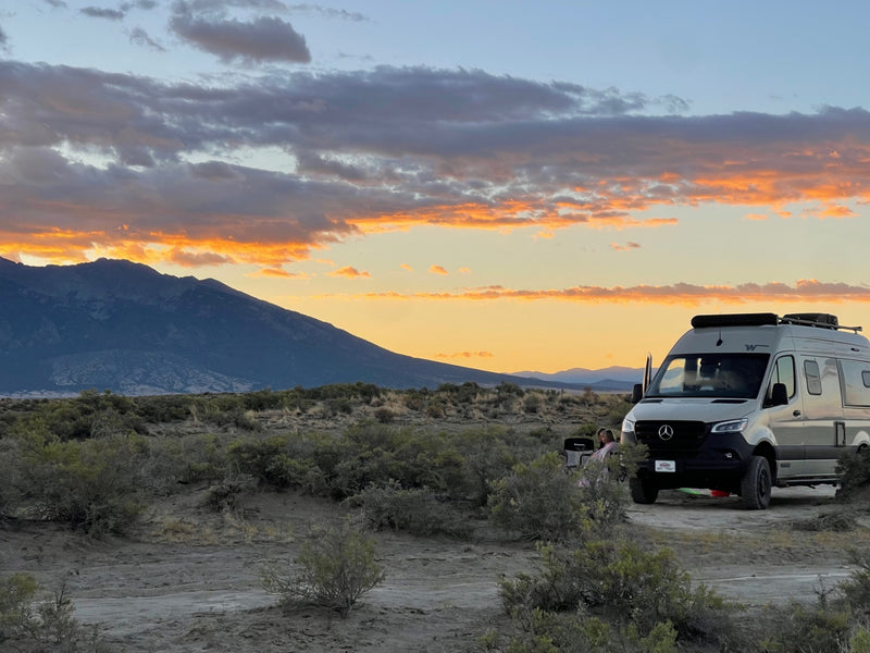 An RV rental parked amidst desert brush during a vivid orange sunset, mountains in background, people relaxing. Great outdoor travel. — photo 5