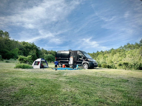 A family enjoys an RV rental camping adventure in a spacious grassy field, with a tent set up next to their camper van.