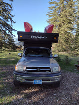 An RV rental: a grey Toyota Tundra truck with a black Palomino pop-up camper, topped with two red kayaks, ready for outdoor adventure.