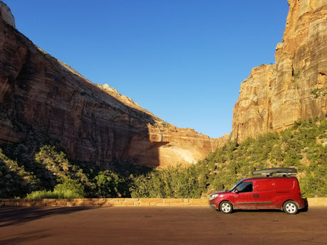 Red **rv rental** van with roof box, parked before towering, sunlit canyon walls. Perfect for **road trips** & **van life**.