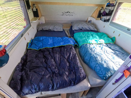 This rv rental shows a cozy sleeping area with two beds, pillows, and sleeping bags, adorned with a 'Life is for adventure' decal.