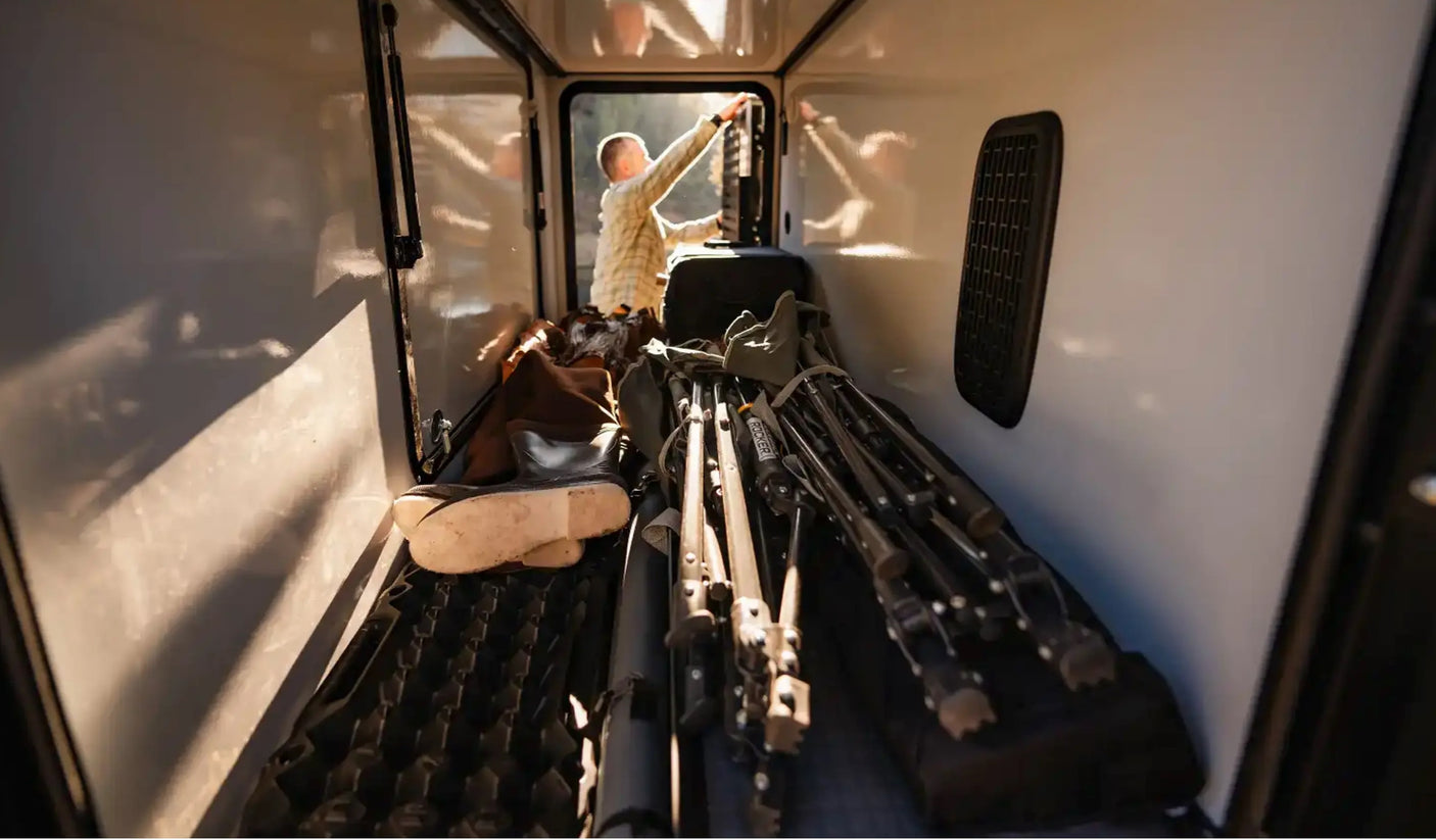 Inside an RV rental cargo area, a person loads hunting rifles & gear. Perfect for outdoor adventures.