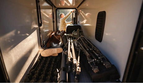 Inside an RV rental cargo area, a person loads hunting rifles & gear. Perfect for outdoor adventures.