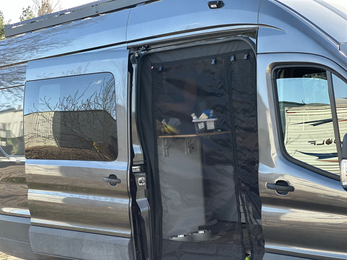 Gray camper van with open side door and mesh screen, revealing an organized interior. Ideal for your next RV rental.