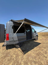 Grey off-road camper van with an extended awning in a dry field, ready for adventure. Perfect for RV rental.