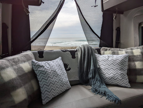 RV rental comfort with ocean views. Relax on plush pillows & blankets, enjoying beach waves from your cozy camper.