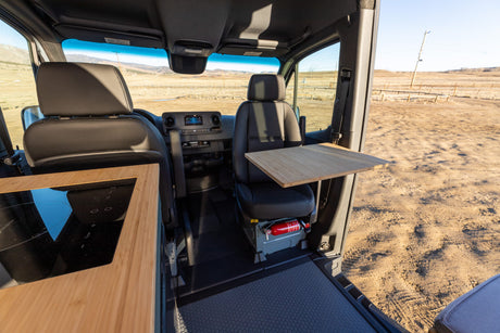 Explore inside an RV rental: Compact camper van interior with an induction cooktop, table, and front seats.