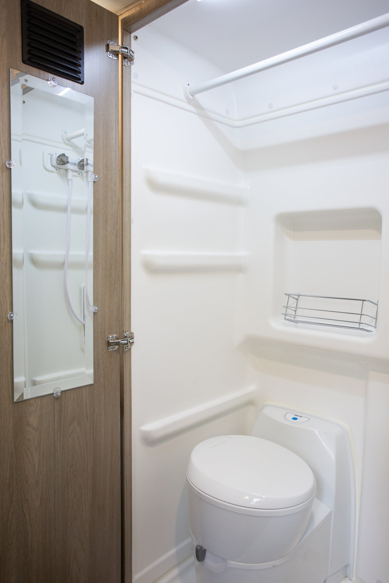 Functional white bathroom in an RV rental, featuring a toilet, shower, and a mirror on the adjacent wall.