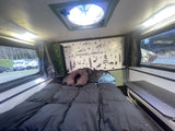 Relax in this cozy rv rental bed with an 'Adventure Awaits' wall. Perfect for travel exploration and comfortable stays.