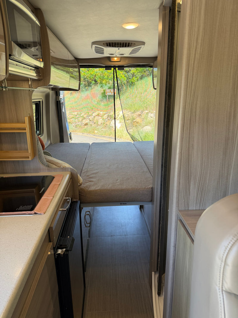RV rental interior: kitchenette, bed, and open rear doors with a mesh screen leading to a scenic outdoor view. — photo 12