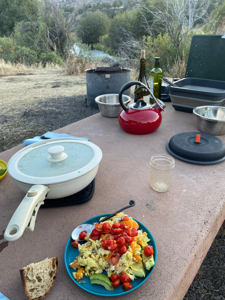 Scenic RV rental campsite breakfast: Eggs, tomatoes, and avocado on a picnic table, with a kettle ready for morning coffee.