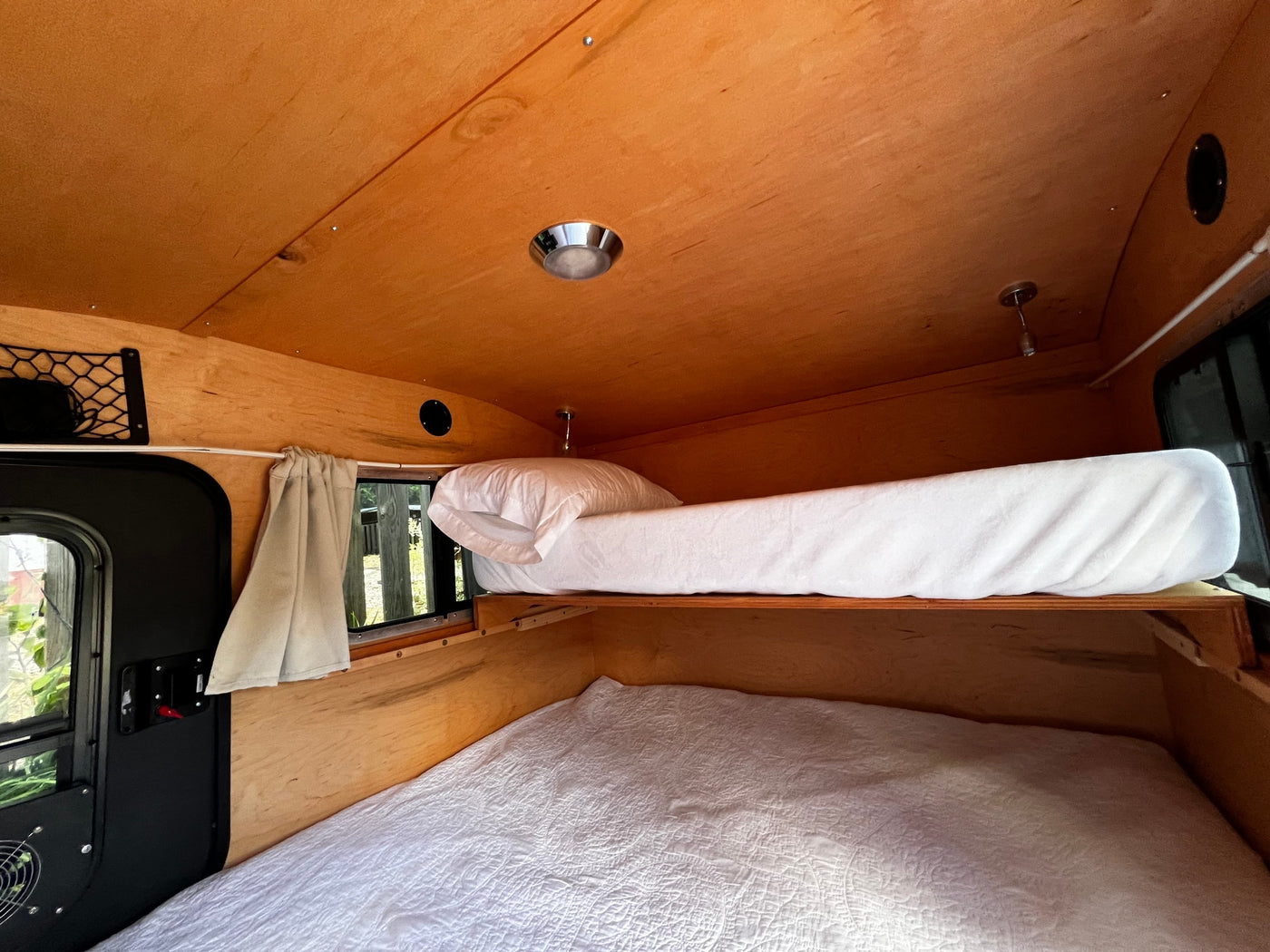 Inside an RV rental, showing a compact wooden bunk bed sleeping area with white bedding and light wood paneling. — photo 9
