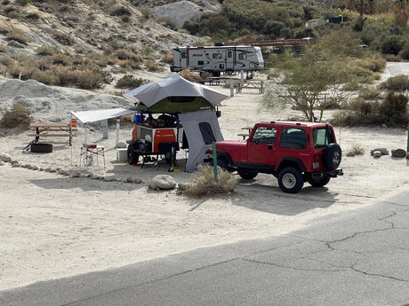 Red Jeep & overland camp setup in a desert campground. An RV rental (Nash) is visible in the background.