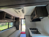 This RV rental interior offers a comfy couch, a functional kitchen with sink/stove, and efficient ceiling AC.