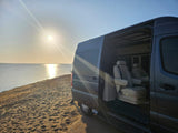 Luxurious RV rental parked on a sandy beach at sunset, showcasing plush interior seats by the tranquil water.
