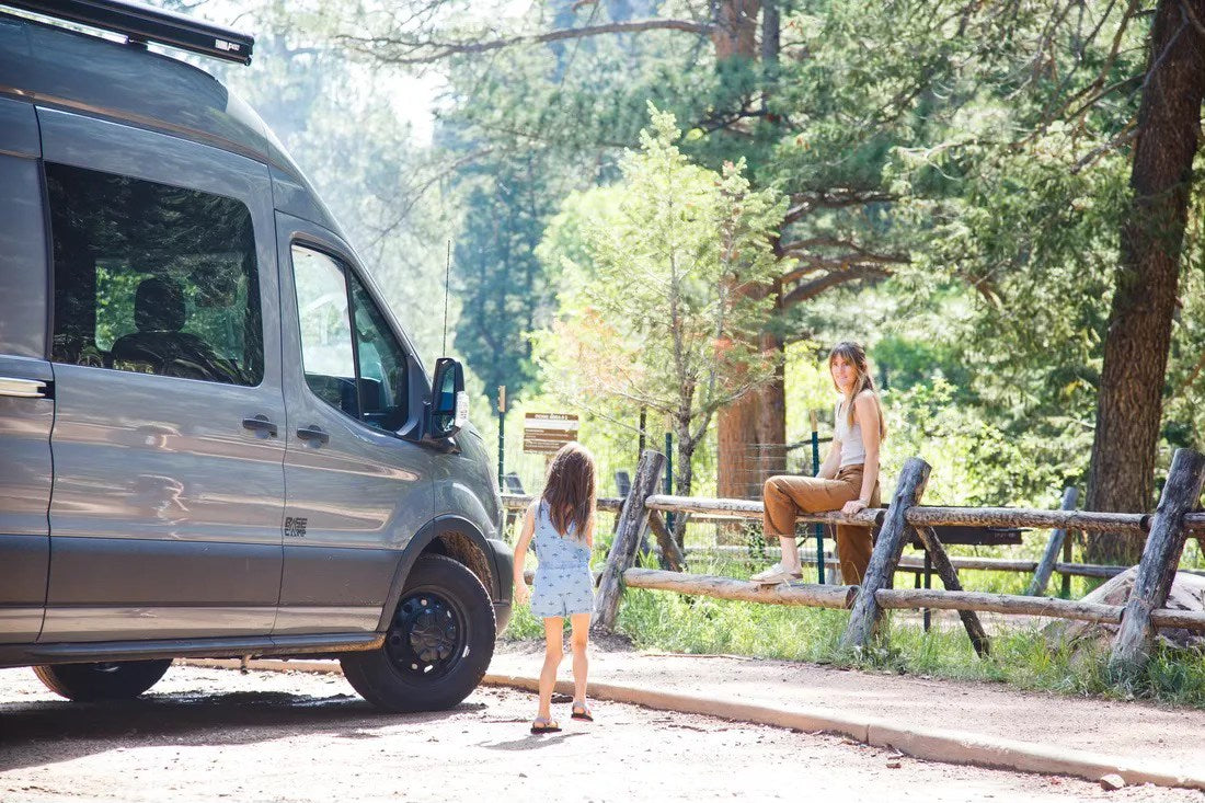  ready for winter adventure.|Explore with an RV rental! A grey camper van and family enjoying a sunny forest setting by a wooden fence.|Rear view of an RV rental: features a high bed platform with stacked mattresses — photo 3