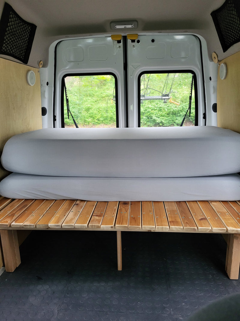  looking forward from the back over a grey sleeping platform to the front seats and dashboard.|Cozy camper van interior with a bed and pillows — photo 9