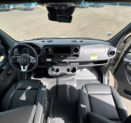 Inside an RV rental: view of the driver's cabin with modern dashboard, steering wheel, and front seating area.