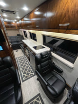Luxury rv rental interior with a compact kitchen, plush black leather seats, and warm wood cabinetry. Perfect for travel.