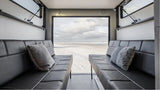 RV rental: Plush black seating inside, offering a panoramic view of a serene sandy beach and ocean under a cloudy sky.