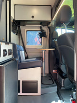 Compact RV rental interior with seating, a small table, overhead storage, and control panel. Well-lit and organized.
