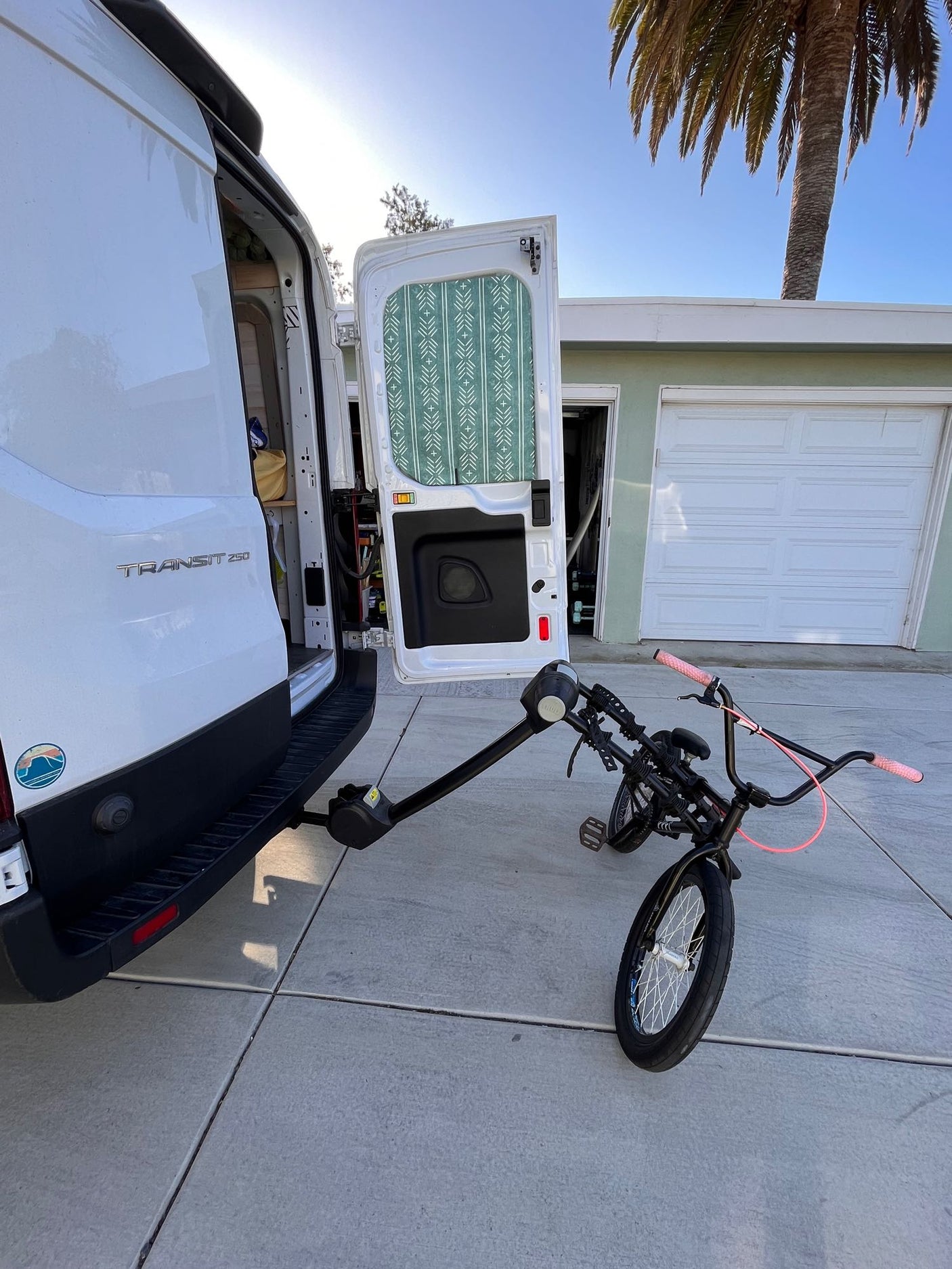 White RV rental van, open doors revealing interior, holds a BMX bike on its rear rack. Ready for adventure on a sunny day.