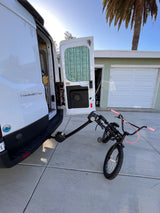 White RV rental van, open doors revealing interior, holds a BMX bike on its rear rack. Ready for adventure on a sunny day.