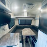 Bright RV rental interior with a U-shaped dinette, overhead cabinets, and TV. Ideal for travel comfort. — photo 16