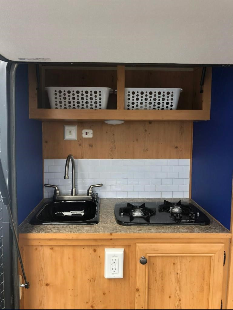 RV rental kitchen: compact setup with sink, two-burner stove, subway tile backsplash, and overhead storage baskets.