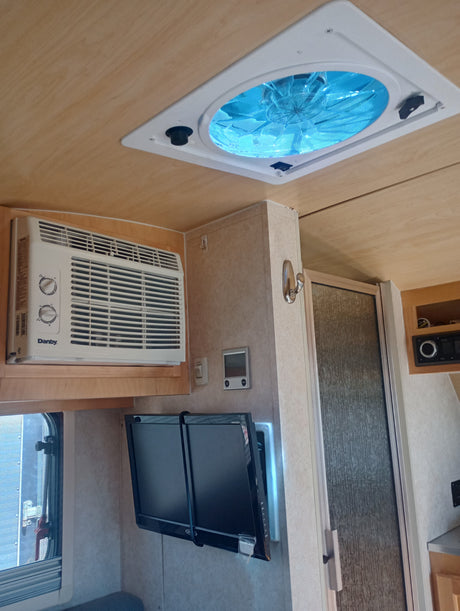 Inside an RV rental: features include a ceiling vent fan, AC unit, dual TVs, and a compact shower.