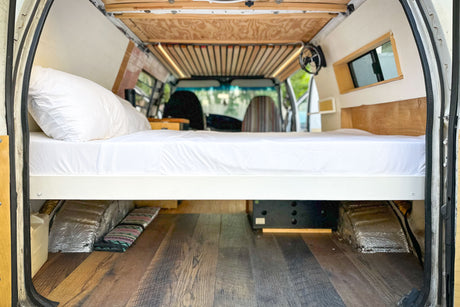 RV rental camper van bed setup. Elevated bed, under-bed storage, and wood flooring. Ideal for van life.