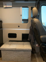RV rental interior featuring a comfortable passenger seat, window with blind, and handy fabric storage ottoman.
