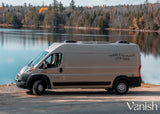 Light beige RV rental parked lakeside, autumn trees reflecting. The van reads: 'THERE'S NO PLACE LIKE HERE'.