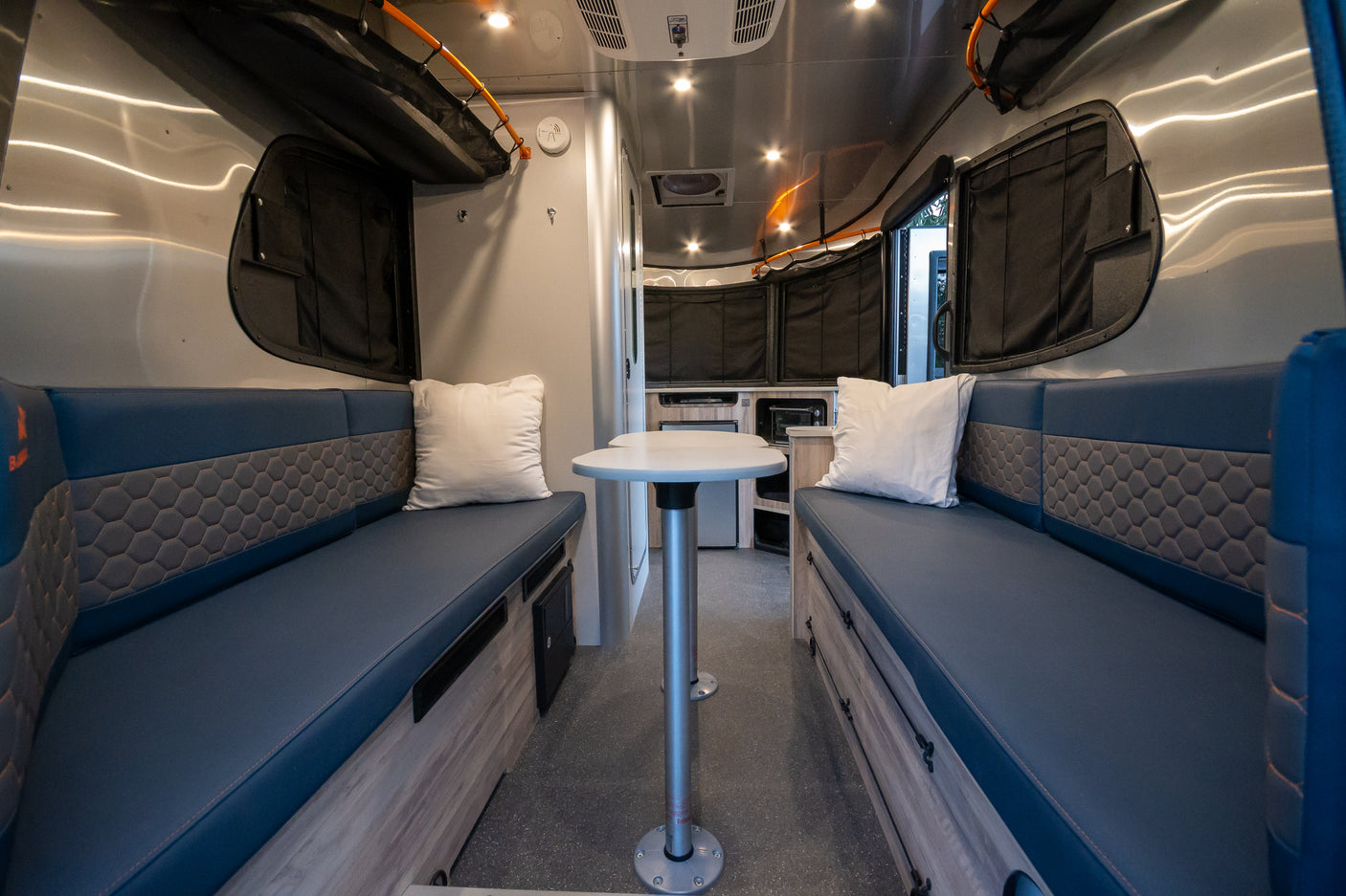 Spacious RV rental interior with comfortable blue benches, a central table, and modern amenities, ideal for travel.