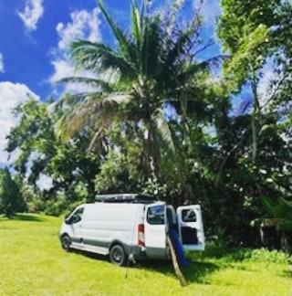  and versatile dining table.|White camper van (RV rental) parked on a sandy beach under a large tree by the ocean. Blue sky above.|A smiling hula girl figurine — photo 7