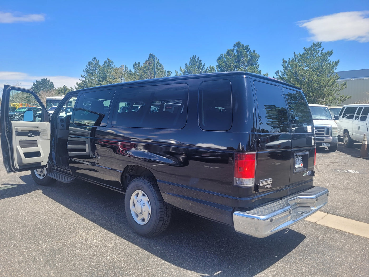 sunny day. Other vans and RVs are visible in the background.|Black Ford E-350 passenger van — photo 2